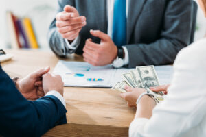A business meeting with professionals reviewing financial documents as one person holds cash, highlighting the role of a qualified appraiser.