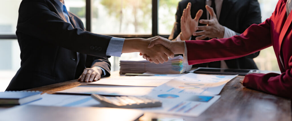 Business professionals shaking hands after a successful mergers and acquisitions valuation agreement at a conference table.