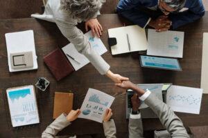 Business professionals shaking hands over financial charts and reports, symbolizing partnership and accuracy in mergers and acquisitions valuation.